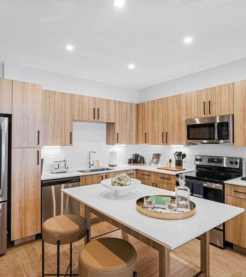 Modern kitchen with wood cabinets, stainless steel appliances, and a white island with two round stools.