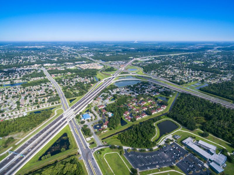 Aerial view of a highway interchange with surrounding neighborhoods, parking lots, and green areas.