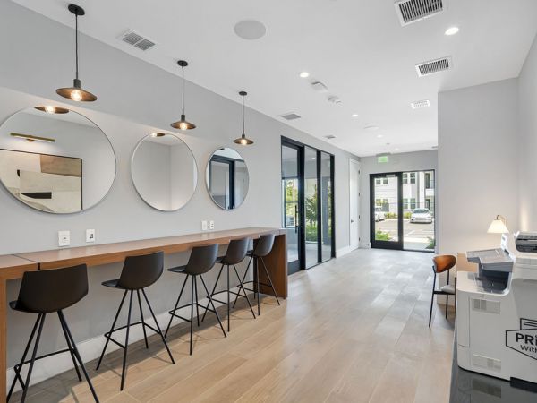 Modern office area with four chairs, round mirrors, pendant lights, and a printer near large windows.