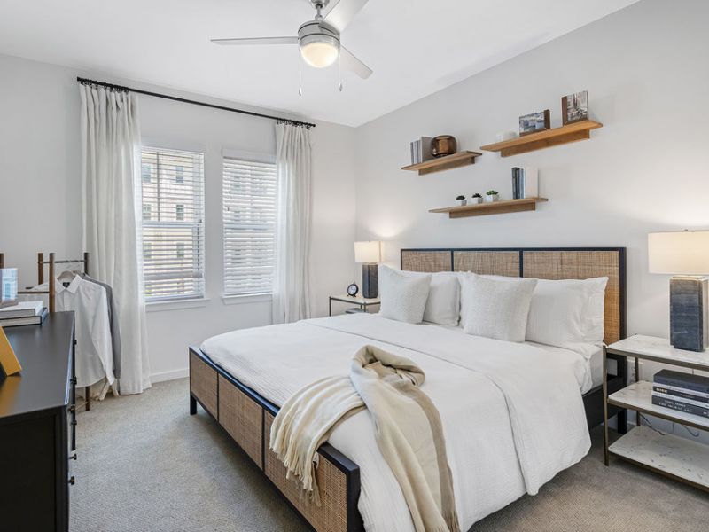 Modern bedroom with a neatly made bed, white bedding, two lamps, and floating shelves on the wall.