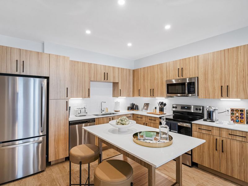 Modern kitchen with wood cabinets, stainless steel appliances, and an island with stools and decor.