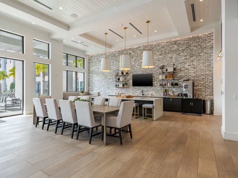 Modern dining and kitchen area with large table, beige chairs, brick wall, and pendant lights.