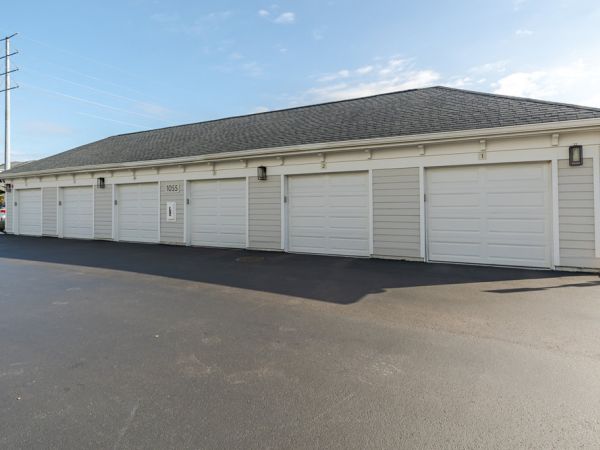 A row of closed white garage doors on a long building with a paved driveway in front.