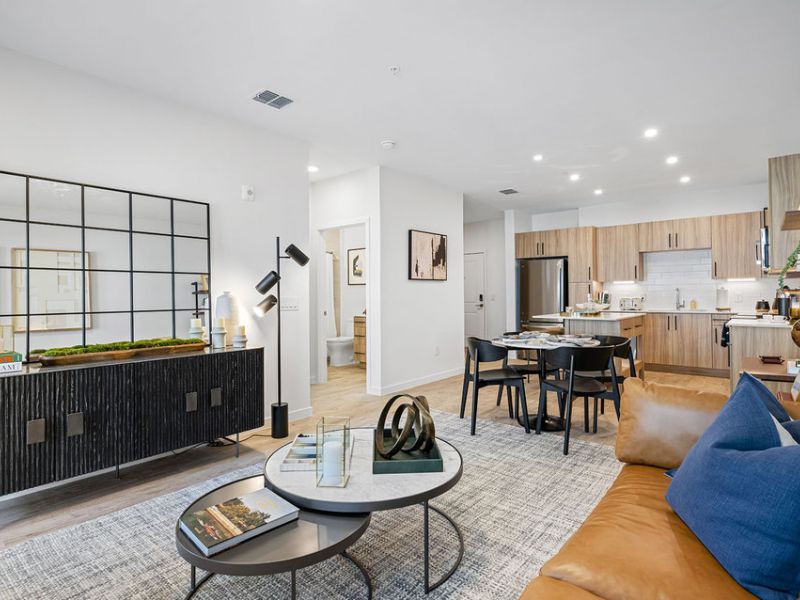 Modern open-concept living room and kitchen with neutral tones, wood accents, and contemporary decor.